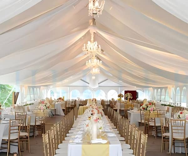 Tables and chairs arranged inside a white marquee with chandeliers